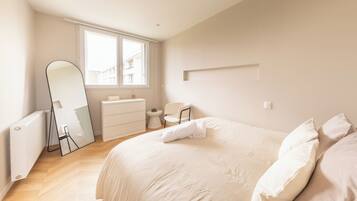 A bedroom with a large bed, a dresser, a chair, a mirror, and a window.