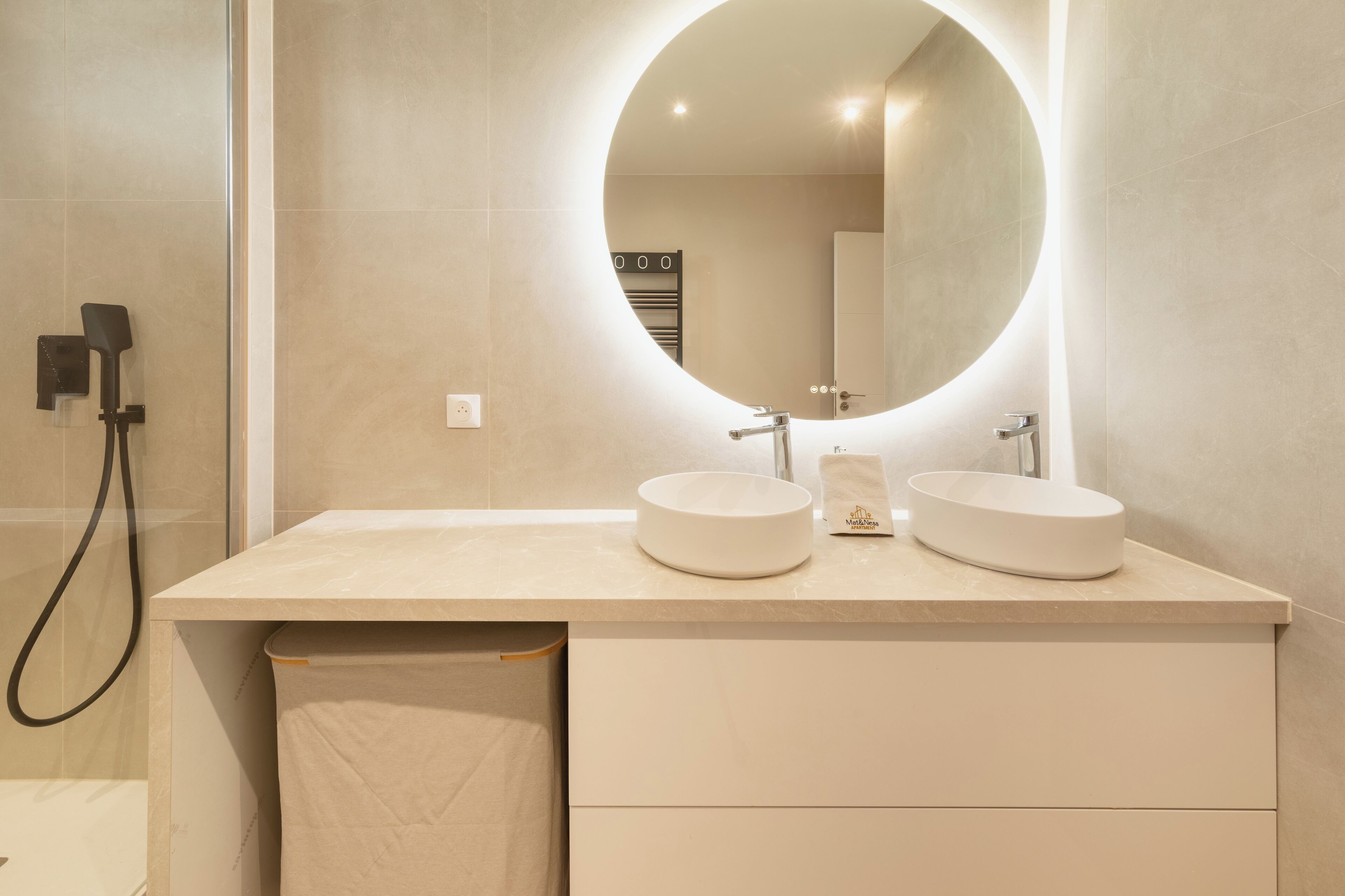 A modern bathroom with two round sinks, a large mirror, and a towel rack.
