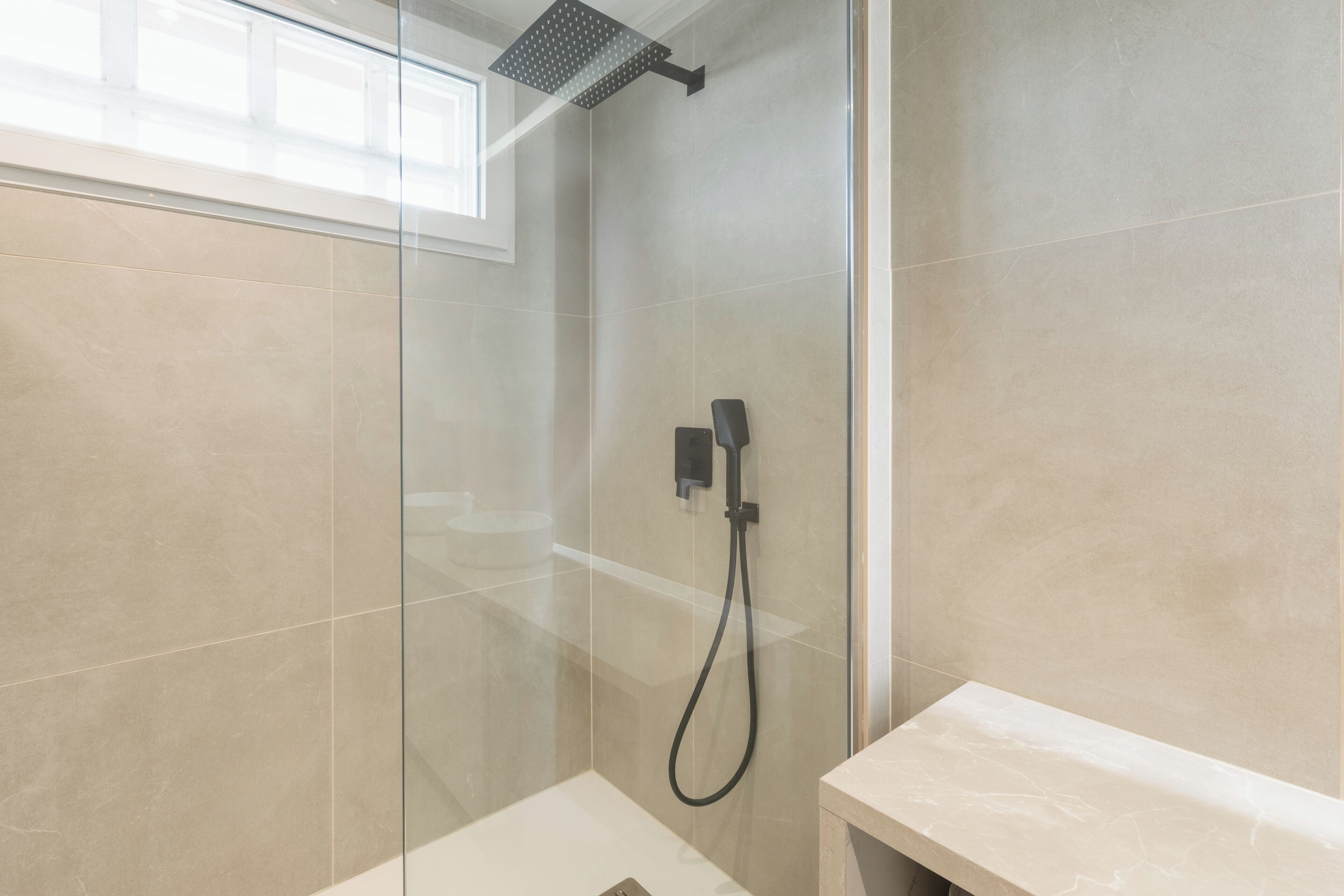 A modern bathroom with a glass-enclosed shower, a white sink, and a marble countertop.