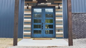 A building with a wooden facade, a blue door, and a deer silhouette. - WhiteTail Cabin with Shuffleboard, Fireplace, WiFi, South of Norman (Purcell)