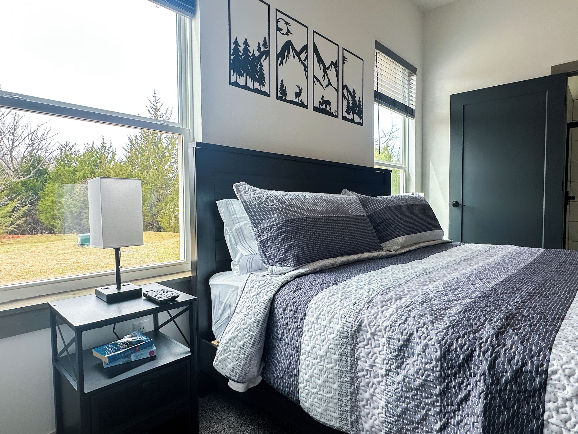 A bedroom with a bed, a nightstand, a lamp, and a window with a view of trees.