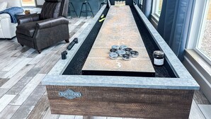 A pool table with a logo, a leather chair, a bar area, and a kitchen in the background. - WhiteTail Cabin with Shuffleboard, Fireplace, WiFi, South of Norman (Purcell)