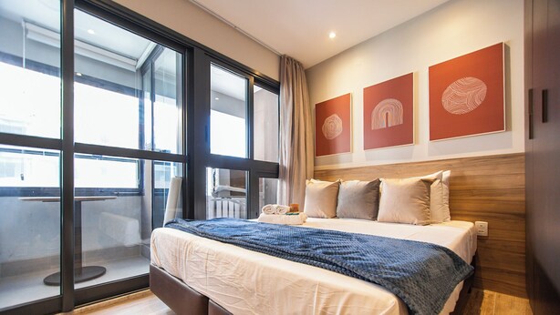 Ett modernt hotellrum med en stor säng, utsikt genom fönster som sträcker sig från golv till tak och tre abstrakta konstverk på väggarna.