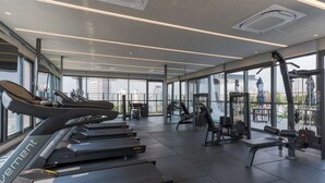 Ett modernt gym med löpband, styrketräningsmaskiner och ett stort fönster med utsikt över staden.