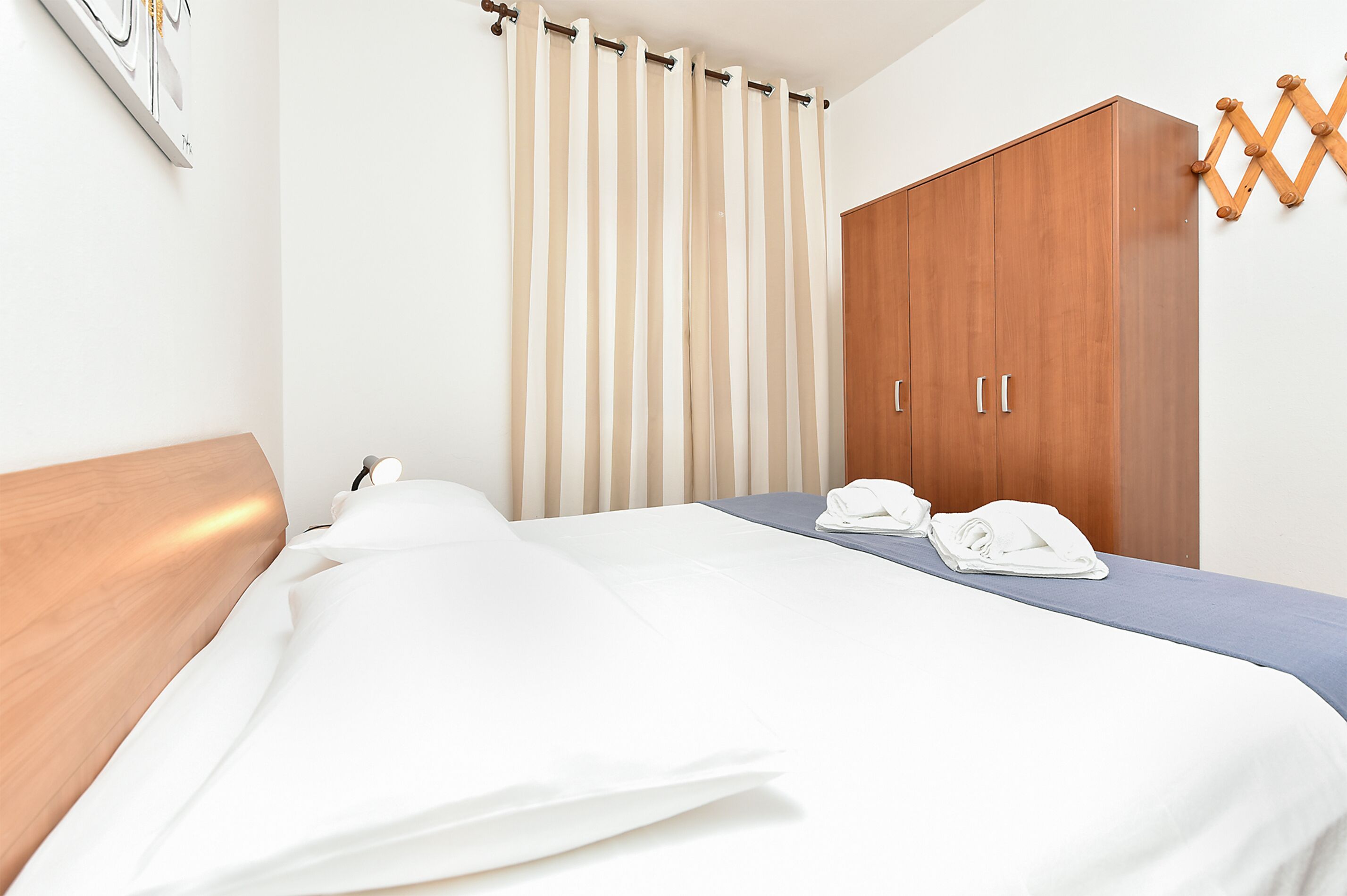 A hotel room with a bed, a wooden wardrobe, and a curtain.