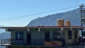 Een gebouw met een bordje voor 'SHIVA Homestay & Restaurant' en waterreservoirs op het dak.