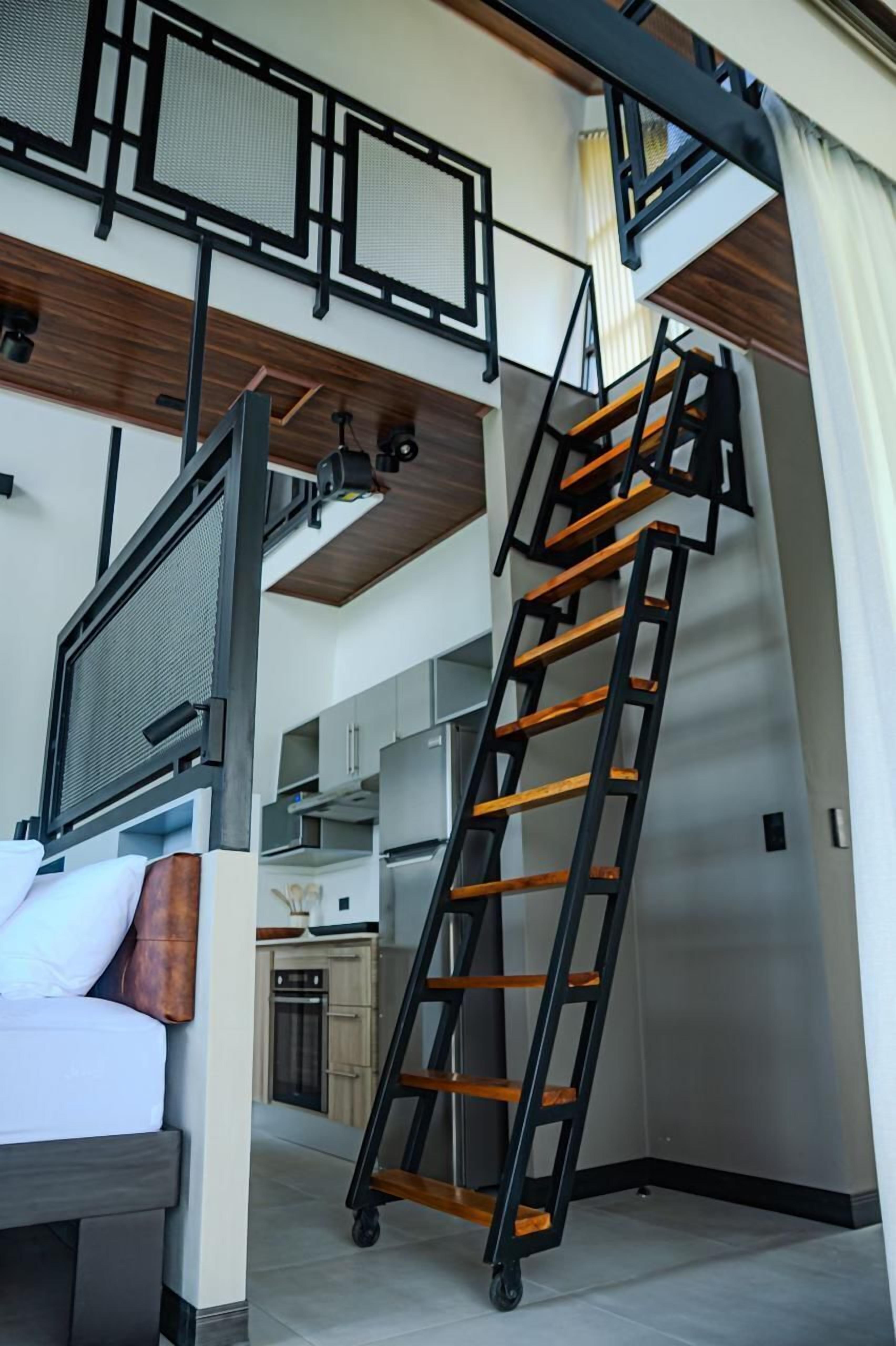 A modern interior with a loft-style bed, a staircase, and a kitchen area.
