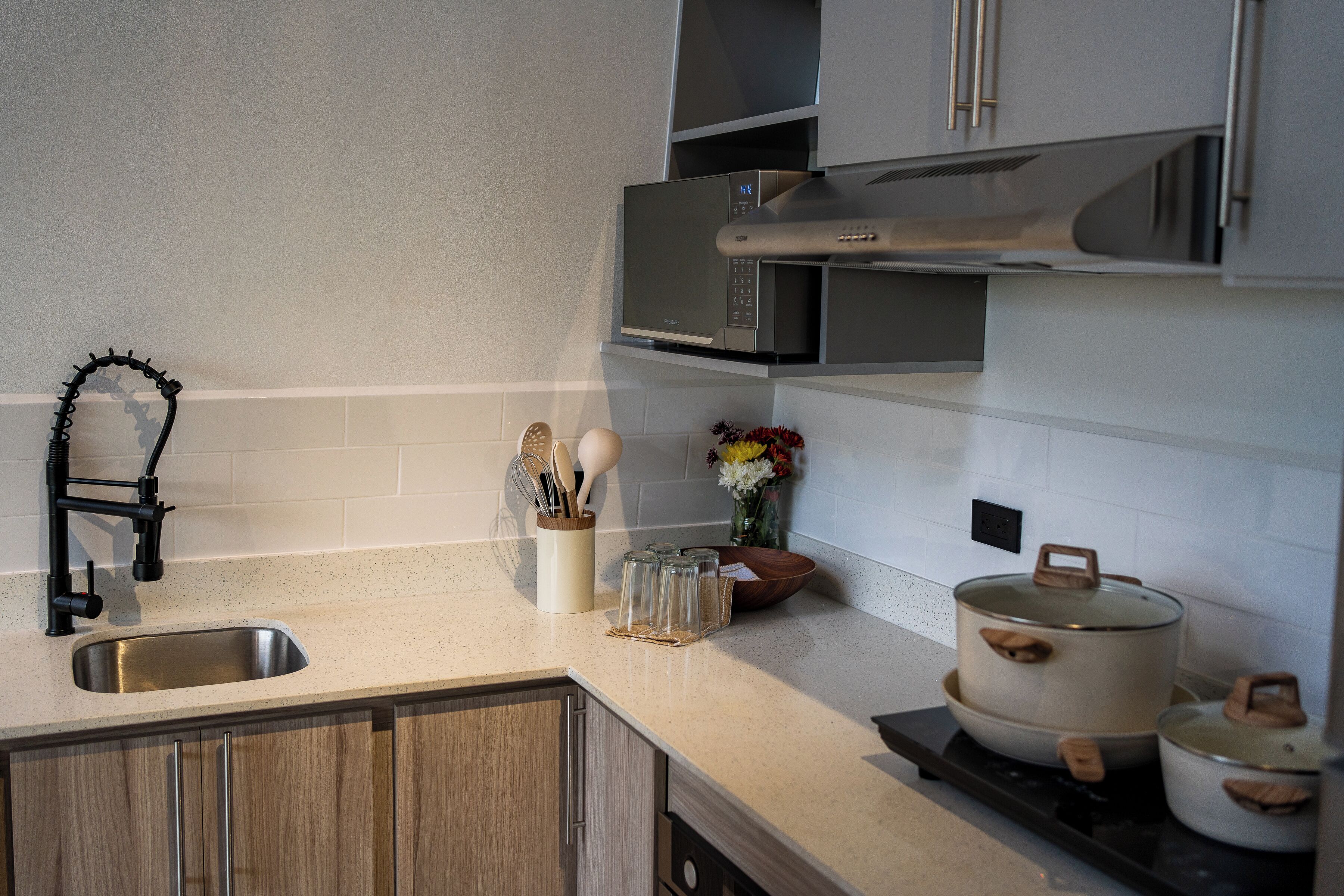 A kitchen with a stainless steel sink, a microwave, a stove, wooden cabinets, and a small black chair.