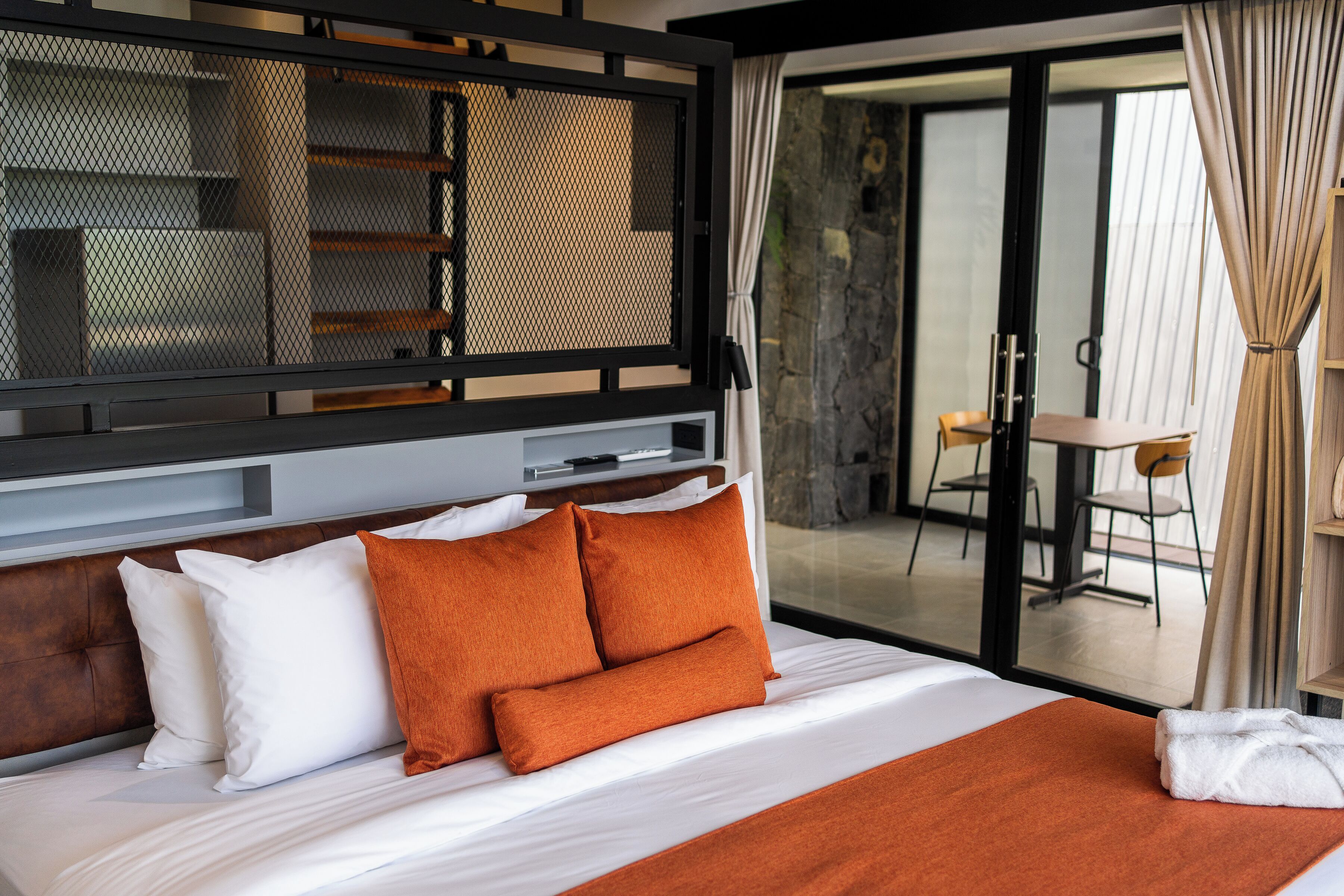 A hotel room with a bed, a headboard, a window with curtains, and a view of the outside.