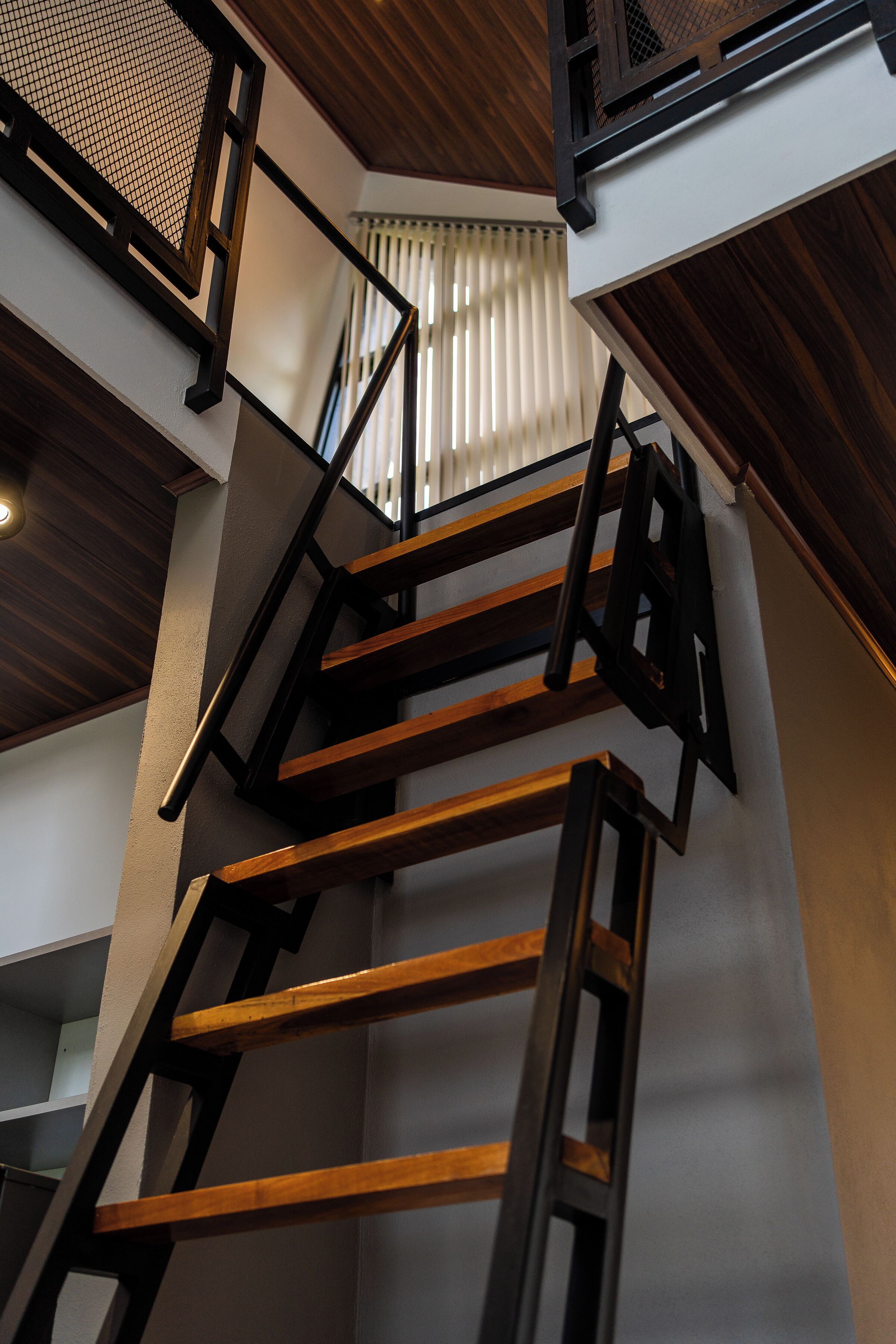A multi-level wooden staircase with a metal railing, white walls, and a wooden ceiling.