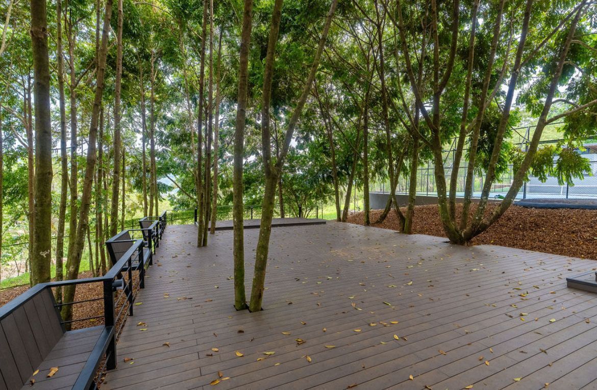 A wooden deck with benches, surrounded by tall trees and a fence.