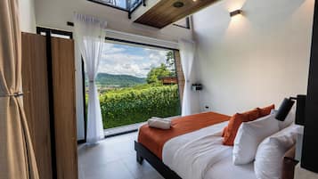 Ein Schlafzimmer mit großem Fenster, einem Bett mit weißer und orangefarbener Bettwäsche und Blick auf grüne Vegetation.