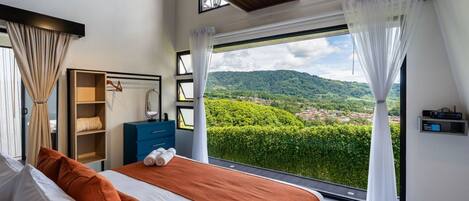 Un dormitorio moderno con una cama grande, un armario, un espejo y vistas a un paisaje verde exuberante a través de amplios ventanales.
