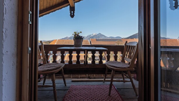 A balcony with two wooden chairs, a table with a potted plant, and a view of mountains.