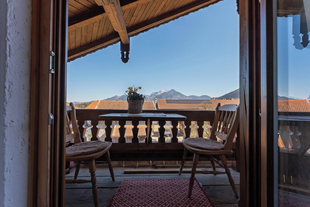 Een balkon met twee houten stoelen, een tafel met een bloempot en uitzicht op bergen.