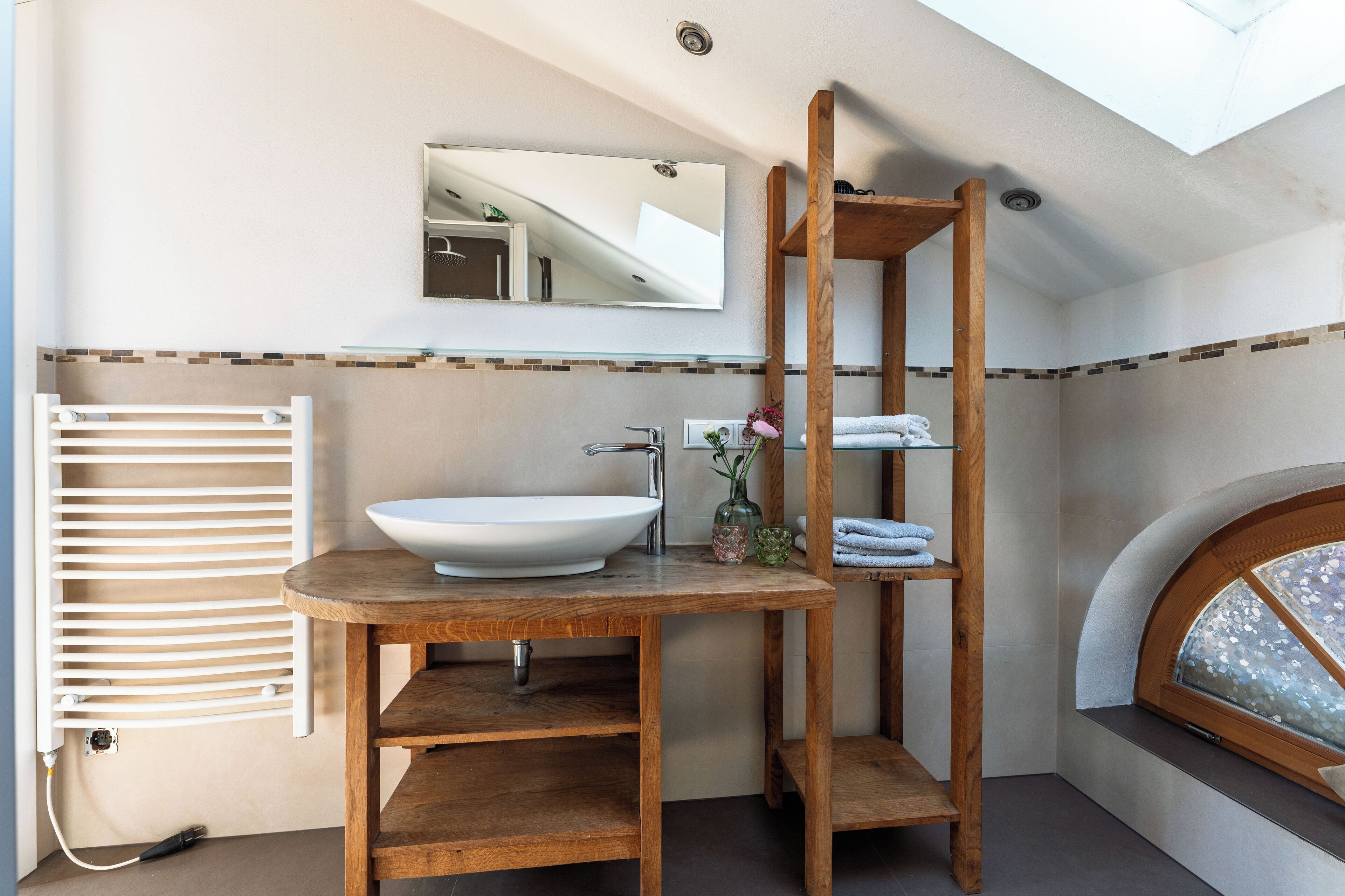 A bathroom with a wooden vanity, a large mirror, a white sink, a towel rack, and a window with a view.