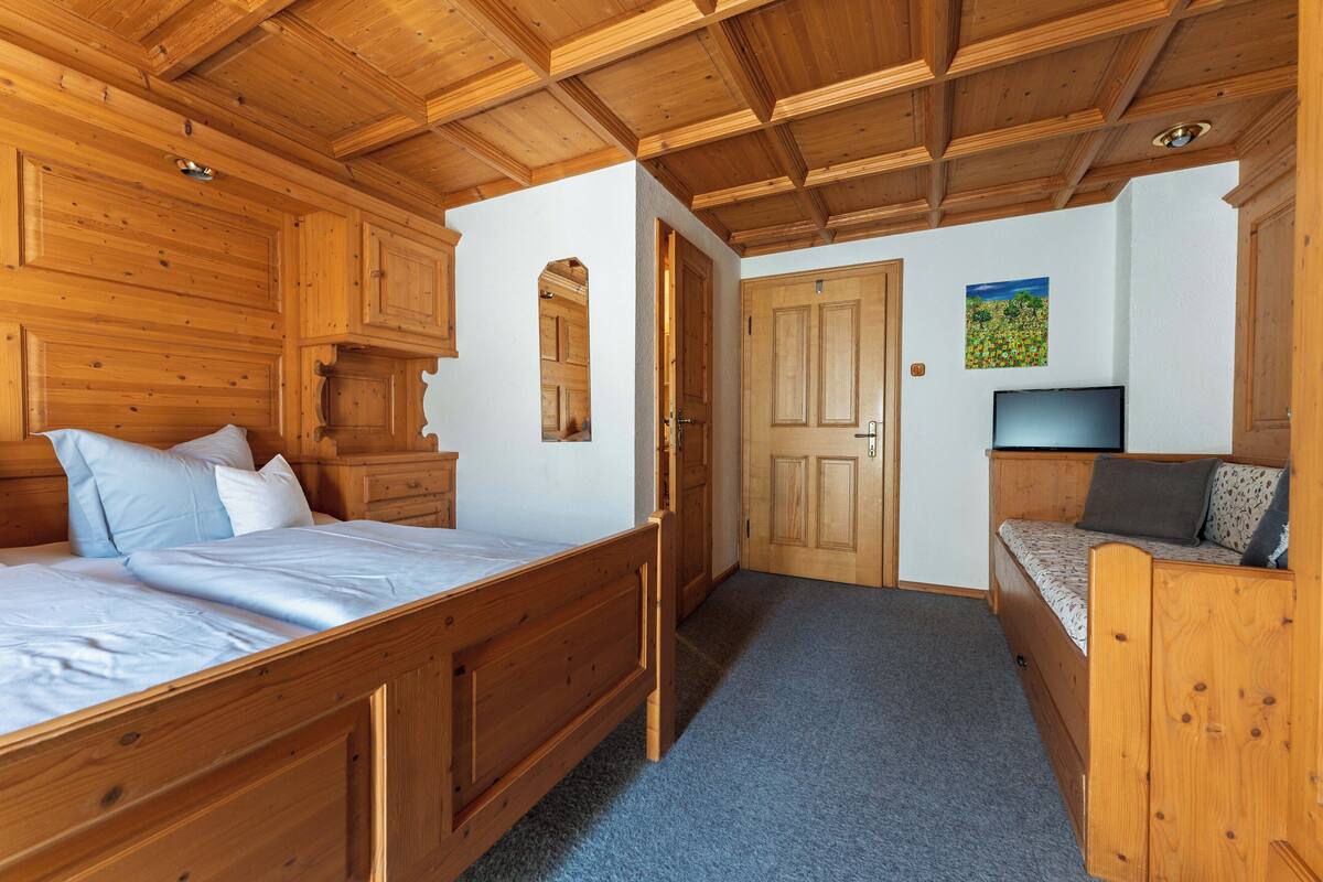 Een slaapkamer met houten details, een bed, een bank en een televisie.
