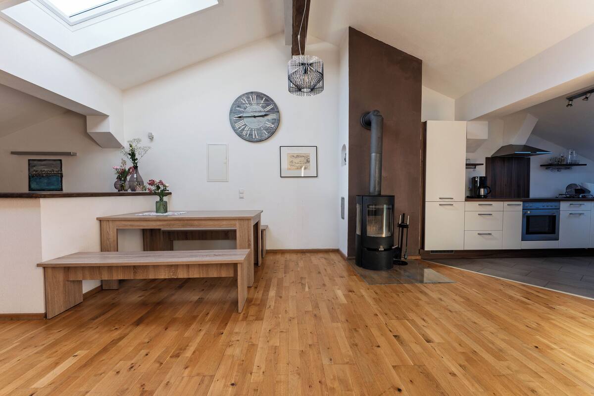 Een moderne keuken met een houten bankje, een grote klok en een houtkachel.