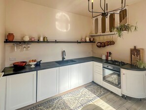 A kitchen with white cabinets, a black countertop, a gas stove, and a hanging pot rack. - 1 bedroom accommodation in Torquay (Torquay)