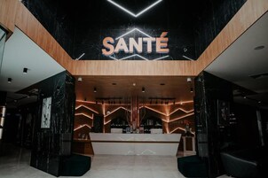 Una moderna zona de recepción con un llamativo letrero 'SANTÉ', detalles de madera y un mostrador de recepción de mármol.