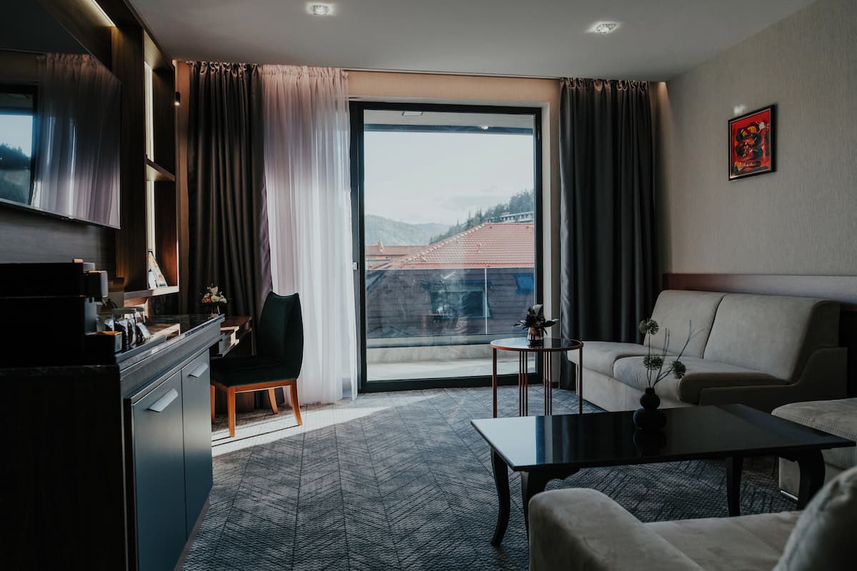 A modern hotel room with a balcony, a sofa, a coffee table, and a dining area.