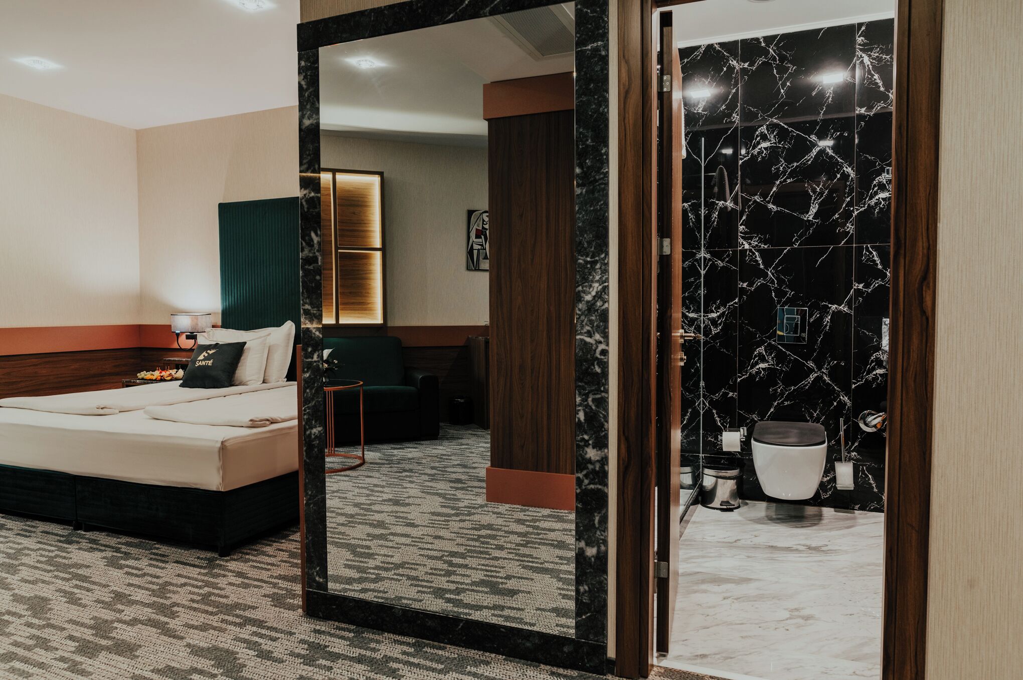 Ein modernes Hotelzimmer mit Bett, einer Sitzecke, einem Badezimmer mit Marmorwand und einem großen Spiegel.