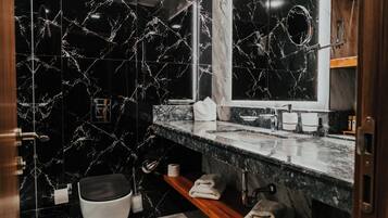 Un baño moderno con paredes de mármol negro, un mueble de tocador de madera, un espejo y un inodoro.