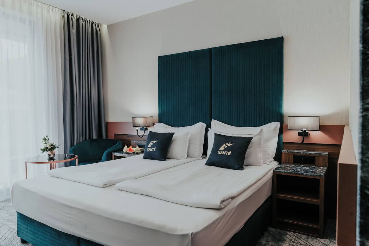 A hotel room with a large bed, two bedside tables with lamps, a chair, and a small table with a vase of flowers.