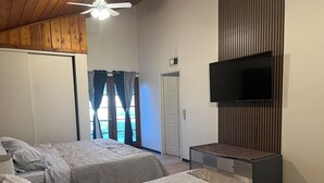 A bedroom with two beds, a ceiling fan, a TV, and a sliding door to a balcony.