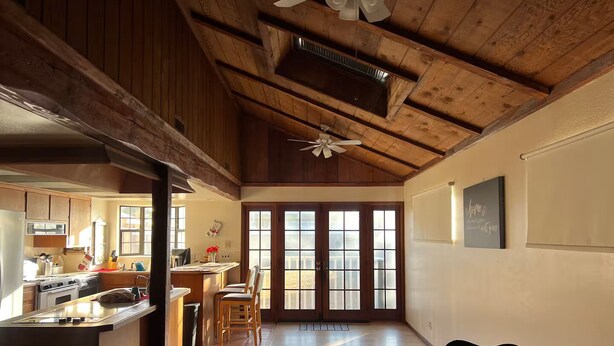 A spacious kitchen with wooden beams, a dining area with chairs, and a large window with frosted glass panels.