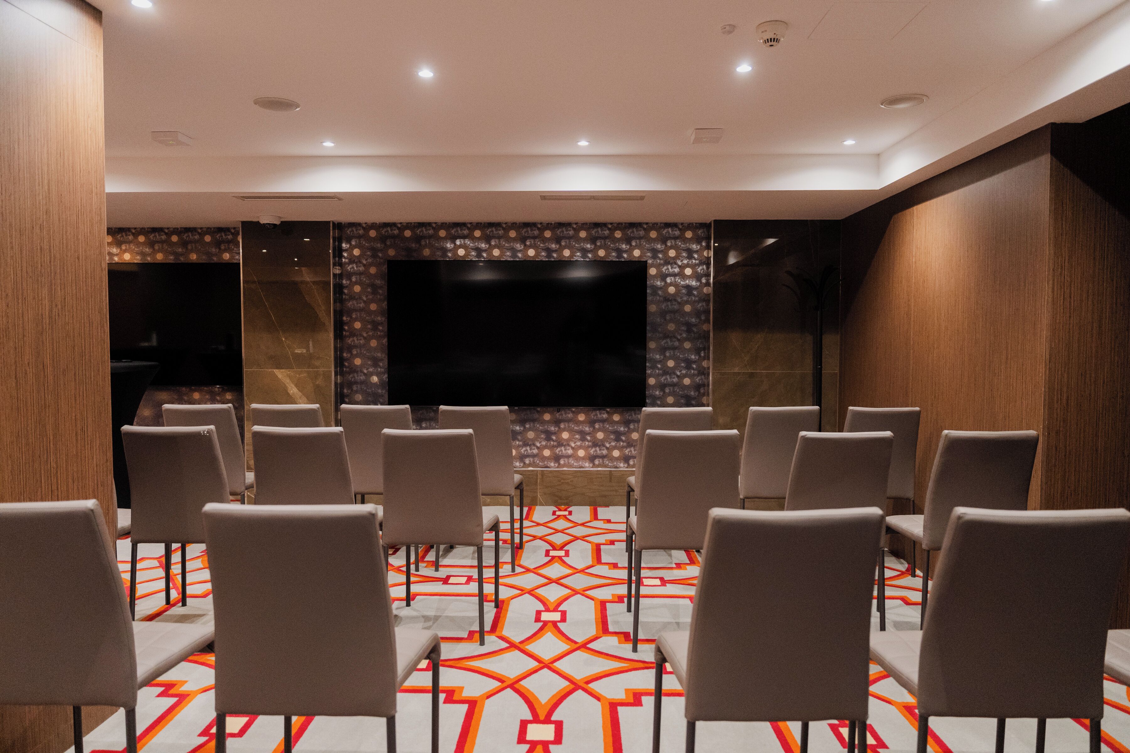 Un salón de conferencias con una gran televisión de pantalla plana, filas de sillas y una alfombra estampada.