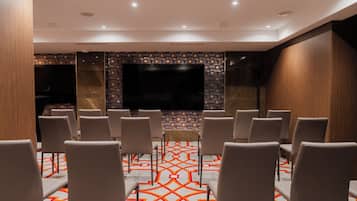 Un salón de conferencias con una gran televisión de pantalla plana, filas de sillas y una alfombra estampada.