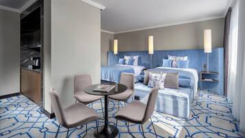 A hotel room with a bed, two bedside tables, a desk with chairs, a round table, and a patterned carpet.