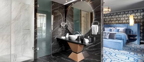 Un bagno moderno con un ampio specchio, piastrelle in marmo nero, un mobile bagno in legno e una cabina doccia separata.