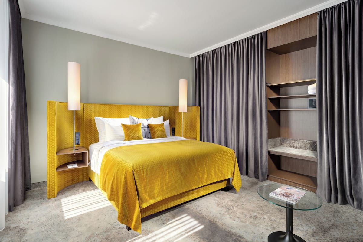 A hotel room with a large bed, a bedside table, a glass side table, and a built-in shelving unit.