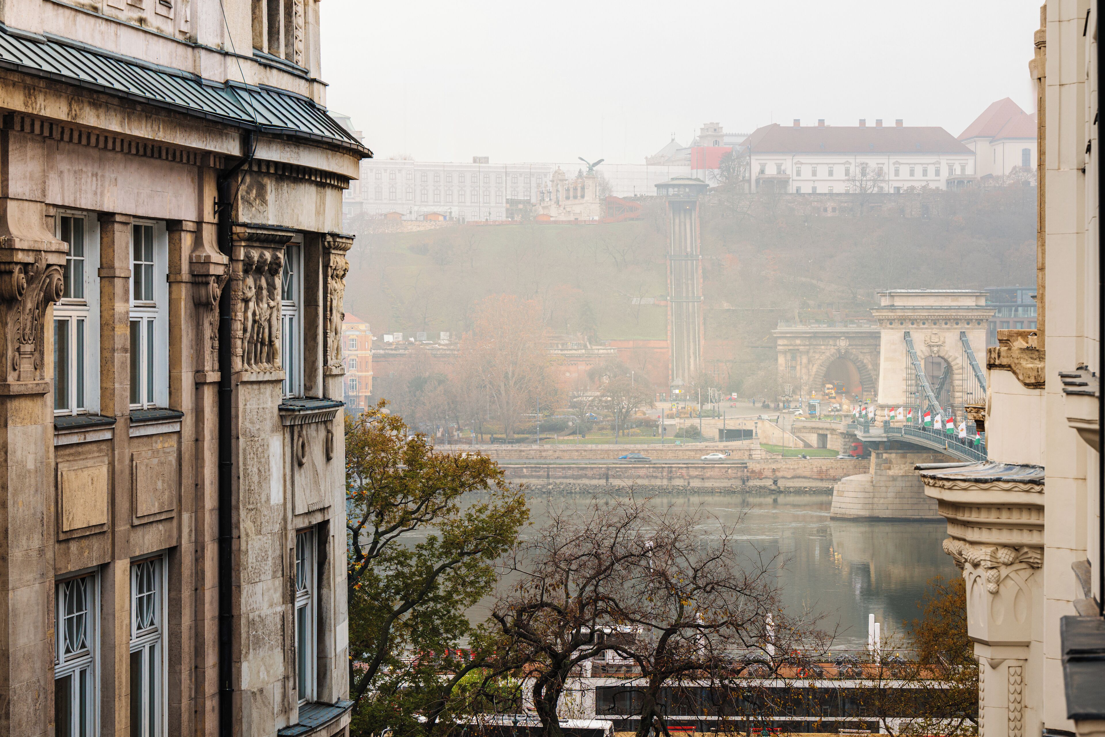 A historic building with classical architecture, a river in the foreground, and a bridge in the background.