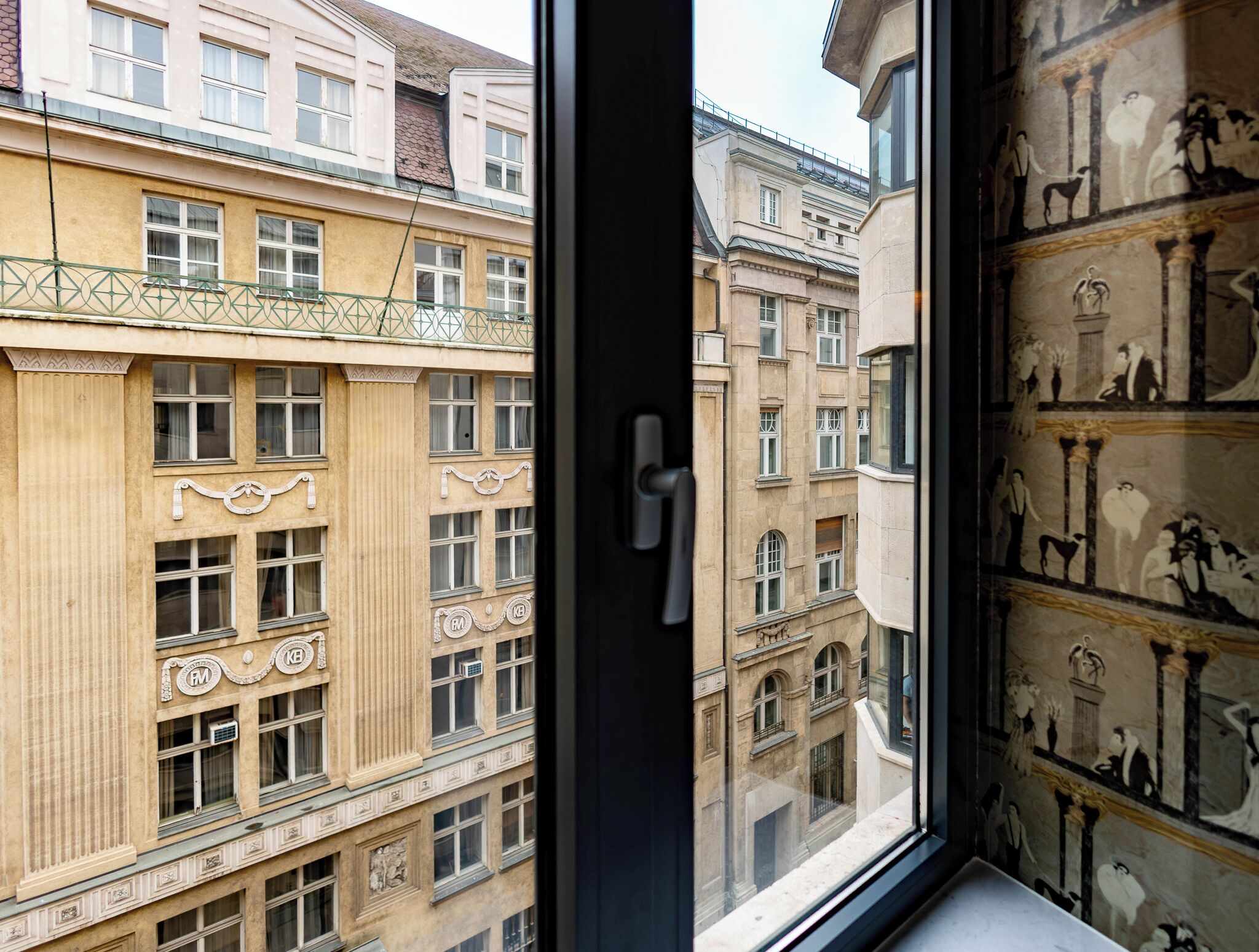 A view through a window of a building with classical architecture, featuring ornate window frames and a balcony with a metal railing.