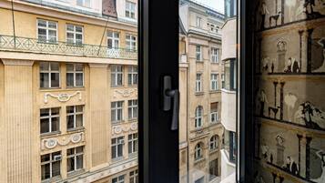 A view through a window of a building with classical architecture, featuring ornate window frames and a balcony with a metal railing.