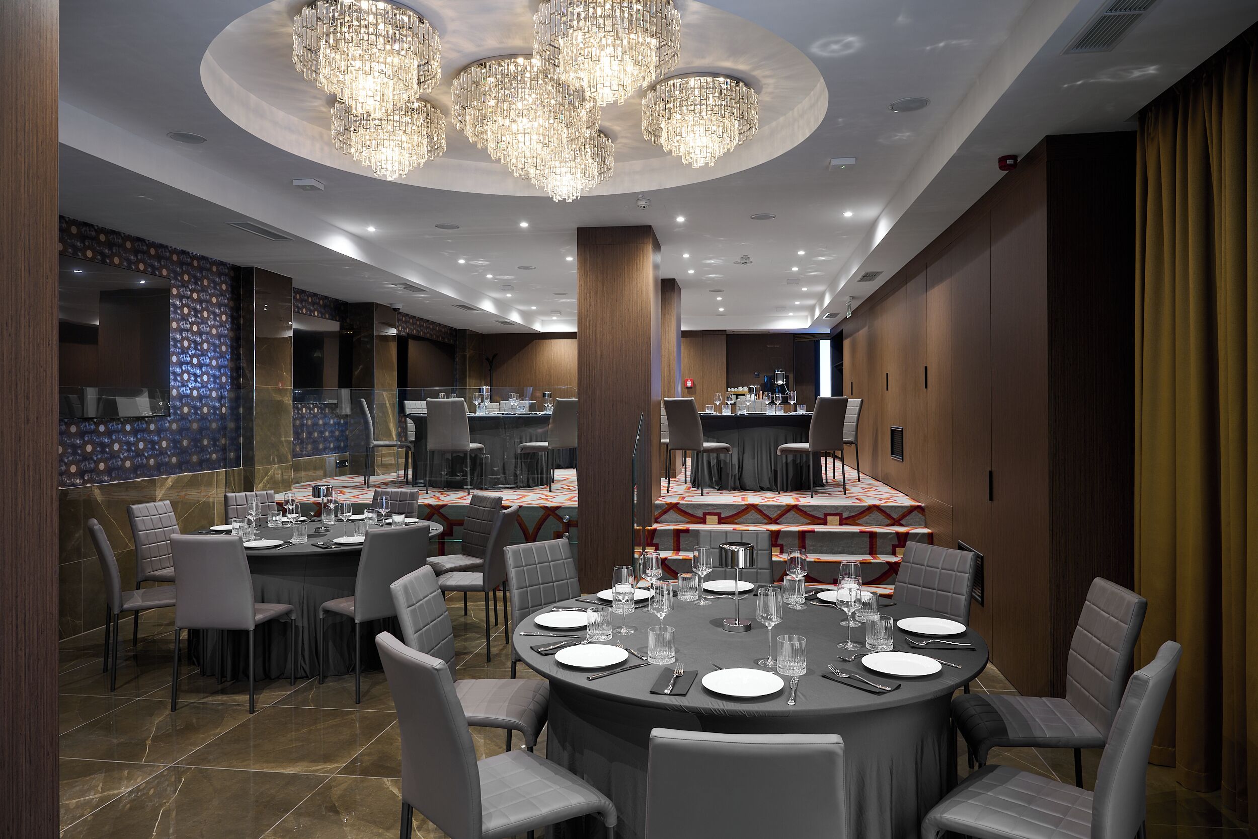 Un espace repas moderne avec des tables rondes, des chaises à revêtement gris et un lustre.