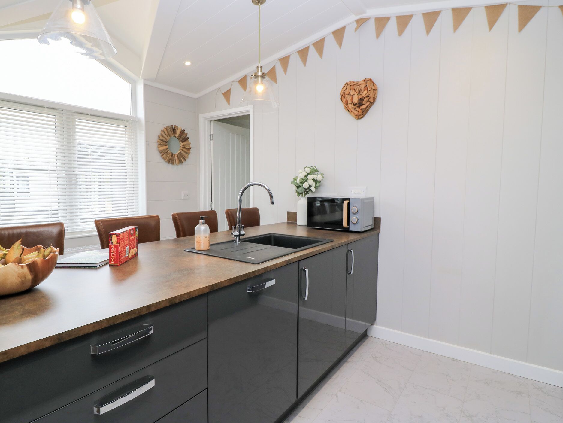 A modern kitchen with a wooden countertop, a sink, a microwave, and a dining area with chairs and a table.