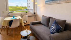 Een woonkamer met uitzicht op zee, een eethoek en een bank met decoratief kussen.