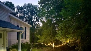 A house with a porch, a gravel pathway, and string lights in the yard. - Modern Marble Montague, NJ/Milford, PA Area Home (Montague)