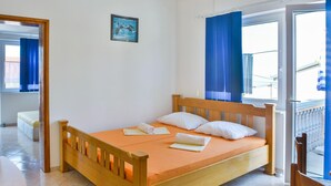 Un lit simple avec un cadre en bois, un matelas blanc et deux oreillers. Il y a une petite table à gauche du lit.