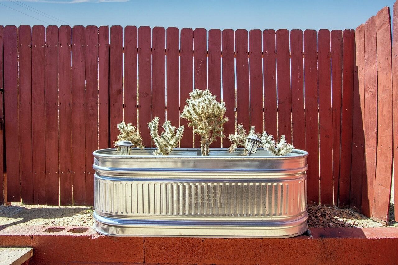A metal planter with cacti against a red wooden fence.