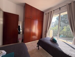 A bedroom with two beds, a wardrobe, a window with curtains, and a balcony.