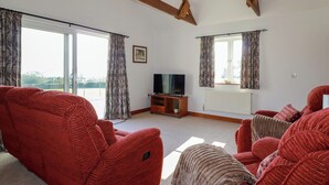 A living room with red sofas, a TV on a wooden stand, and large windows with curtains.