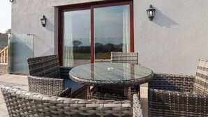 An outdoor seating area with wicker furniture and a glass table, adjacent to a building with a sliding glass door.