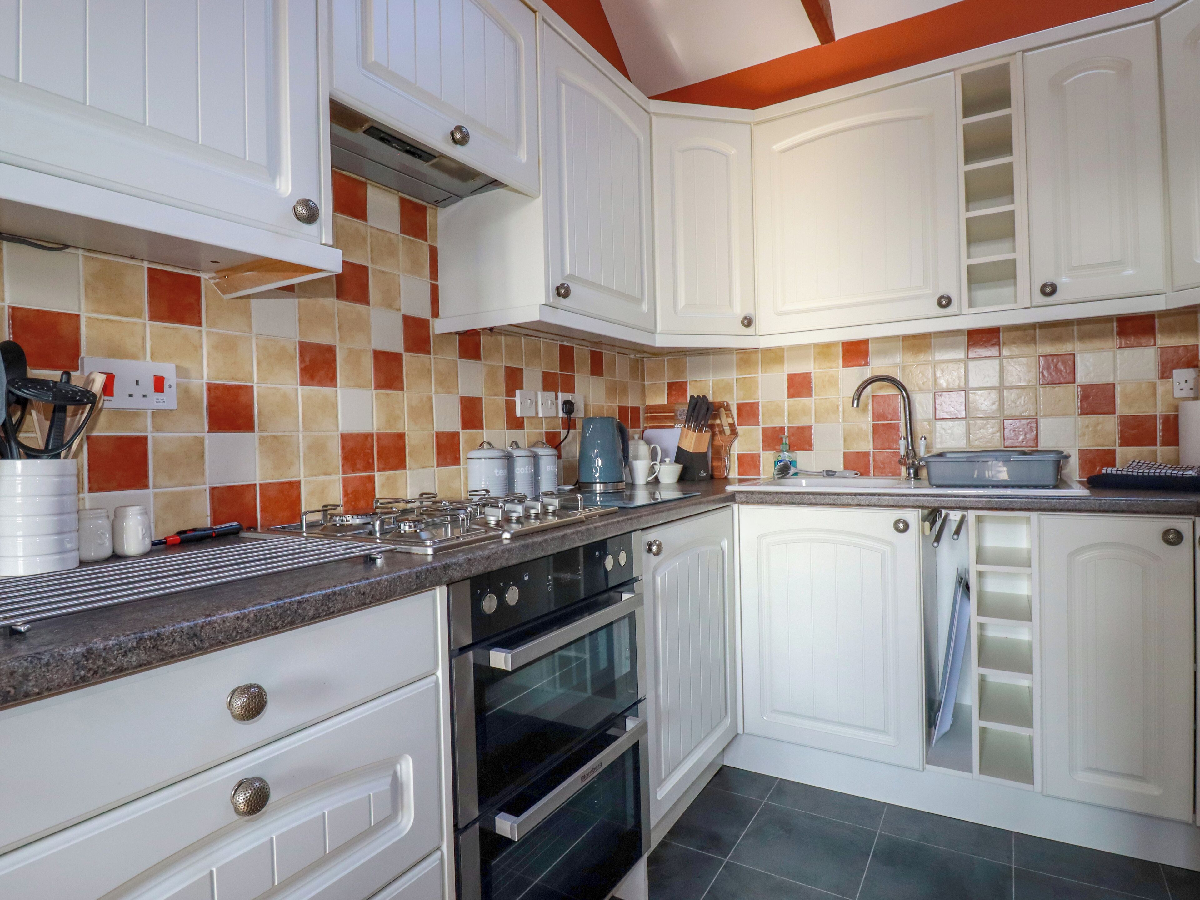 A kitchen with white cabinets, a tiled backsplash, a stove, and a sink.