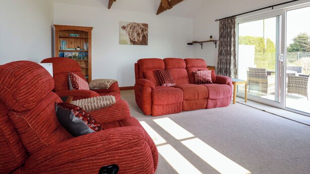 A spacious living room with two red sofas, a wooden bookshelf, and a large sliding glass door leading to an outdoor area.
