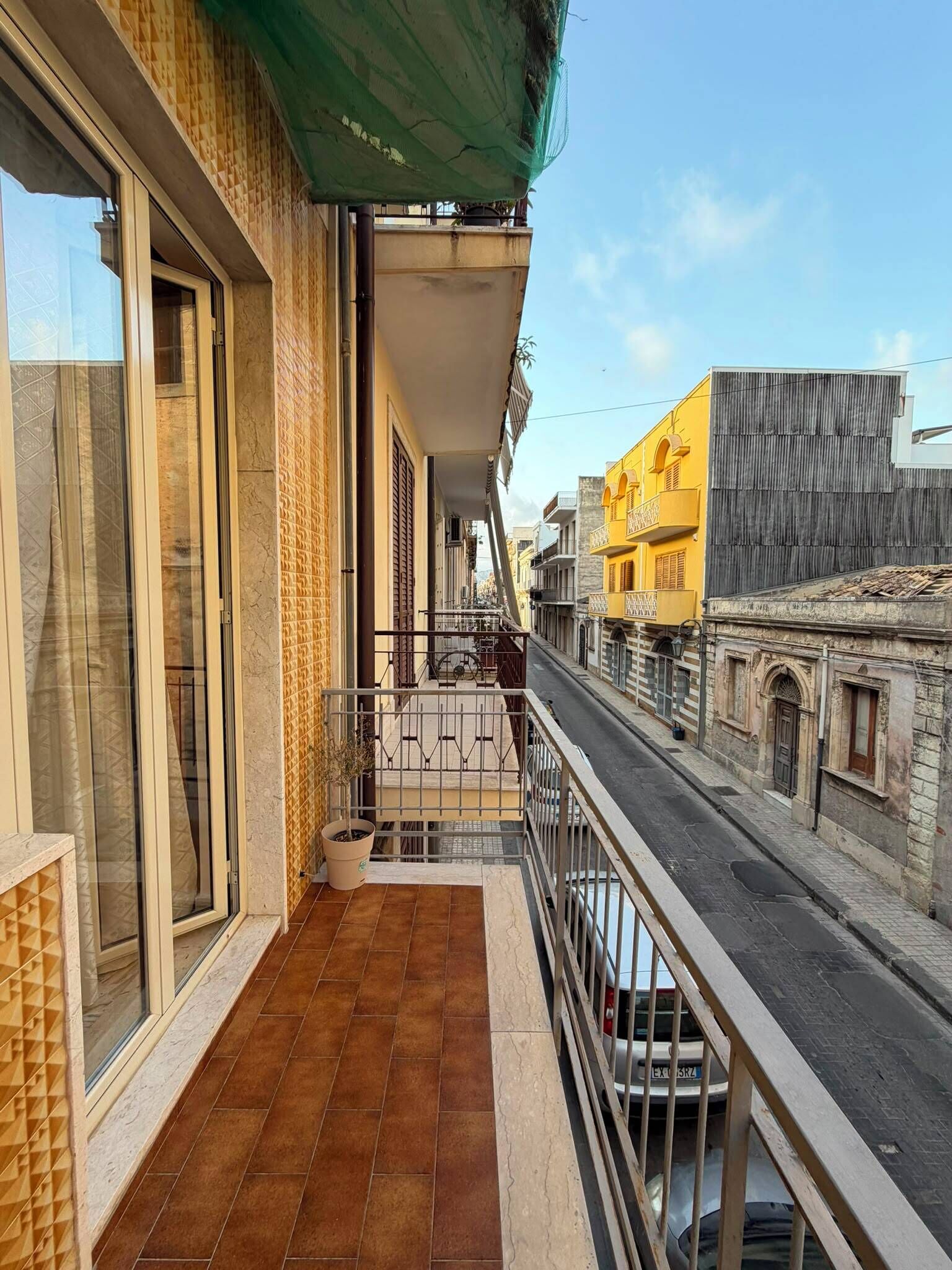 Un balcon donnant sur une rue, un sol carrelé et un bâtiment surmonté d’une marquise verte.